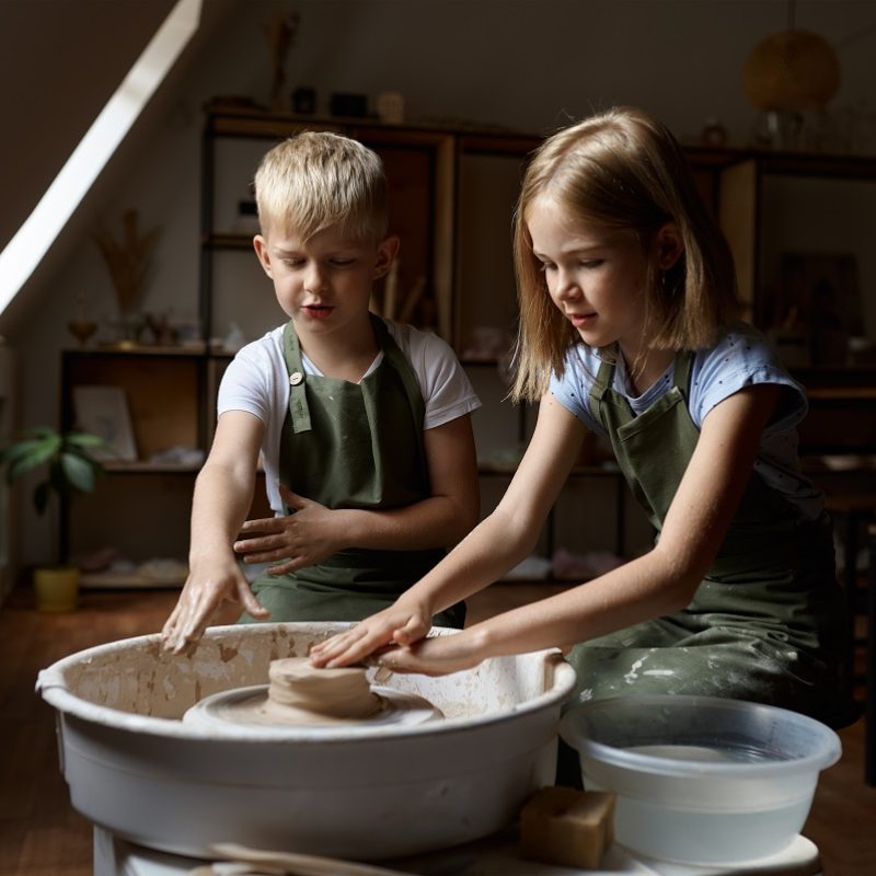 Children work on a potter's wheel in the workshop. Clay modeling lesson at the art school. Young masters of folk crafts, pleasant hobby, happy childhood