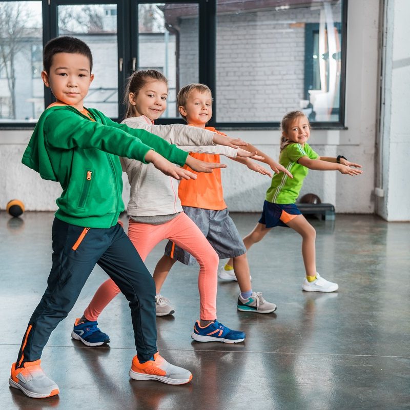 Side view of multiethnic children with outstretched hands doing lunges in gym